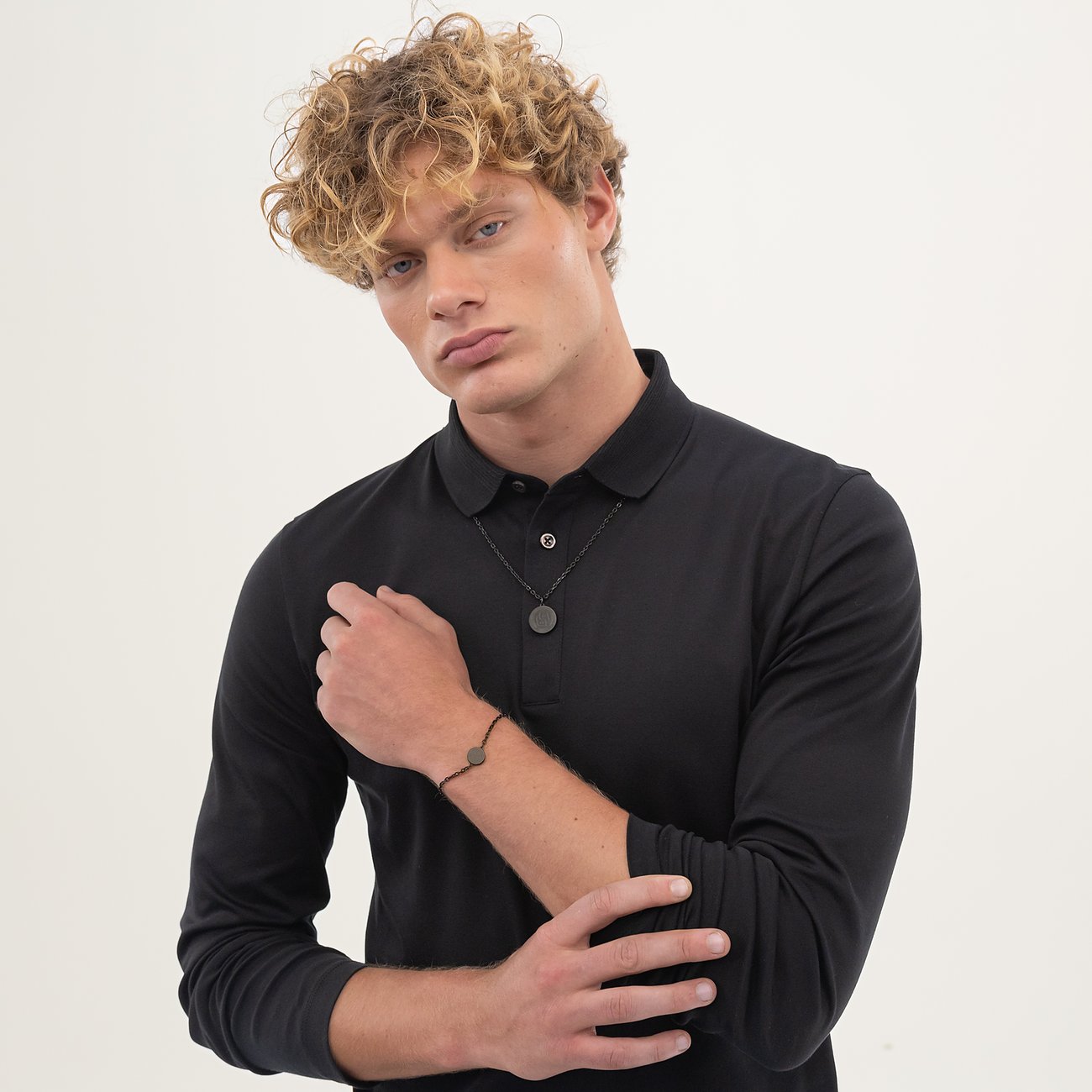 Een jonge man draagt een Boss roestvrijstalen halsketting met ronde hanger en een bijpassende armband.