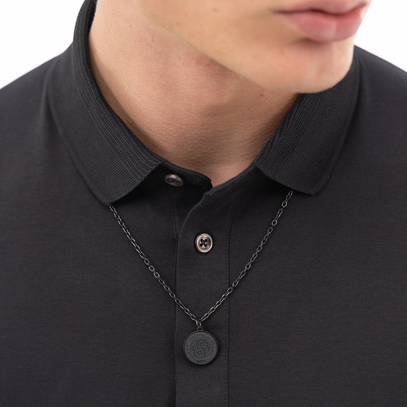 Nauwe detailpersoon draagt een Boss ketting van roestvrij staal met een ronde, donkere hanger.