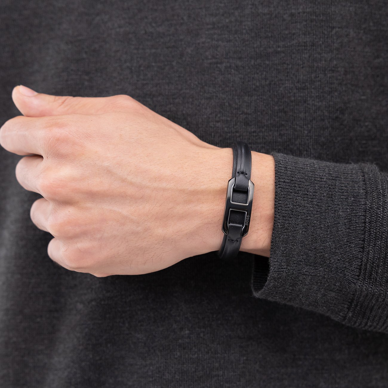Zwarte Boss leren armband met rechthoekige donkere metalen sluiting, gedragen om de pols van een man.