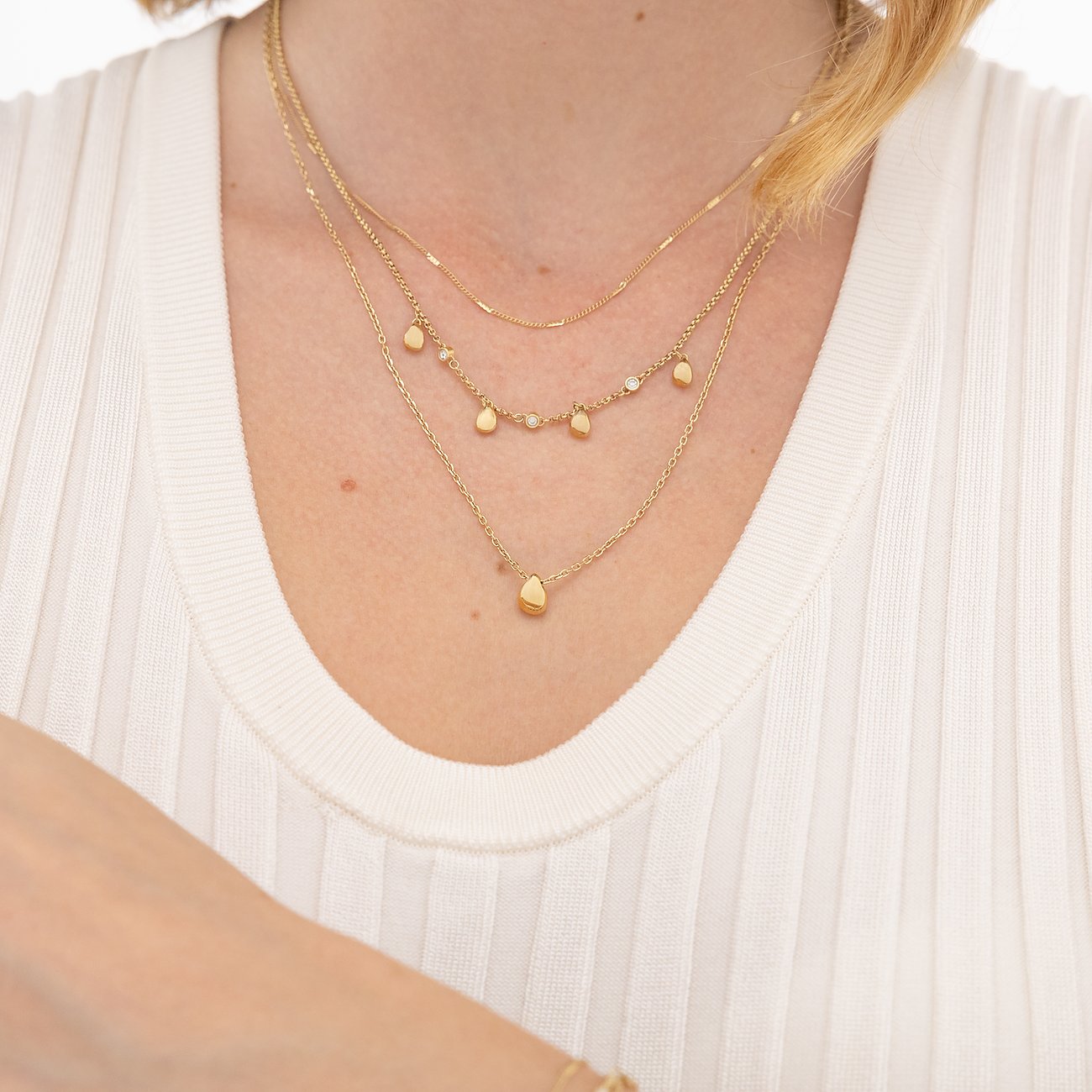 Drei goldene Boss-Halsketten aus Edelstahl am Hals einer Frau. Eine Kette mit tropfenförmigem Anhänger.