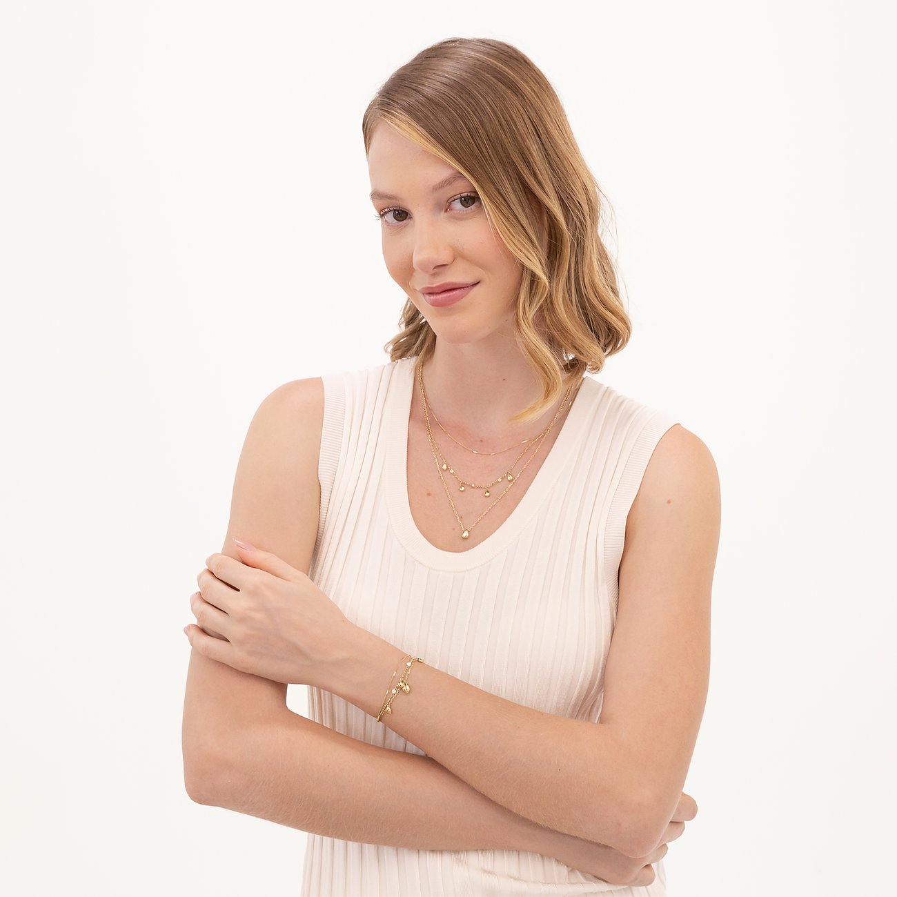 Eine Frau trägt ein Boss Armband aus goldfarbenem Edelstahl mit Herzcharms. Sie trägt auch mehrschichtige Halsketten.