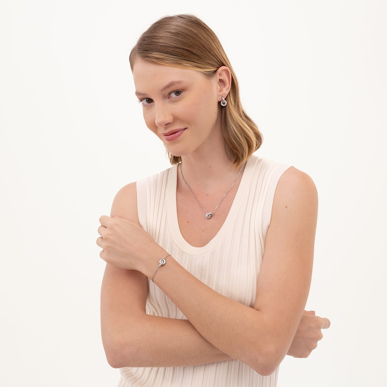 Een vrouw draagt een zilverkleurige Boss sieradenset van roestvrij staal, bestaande uit oorbellen, ketting en armband.