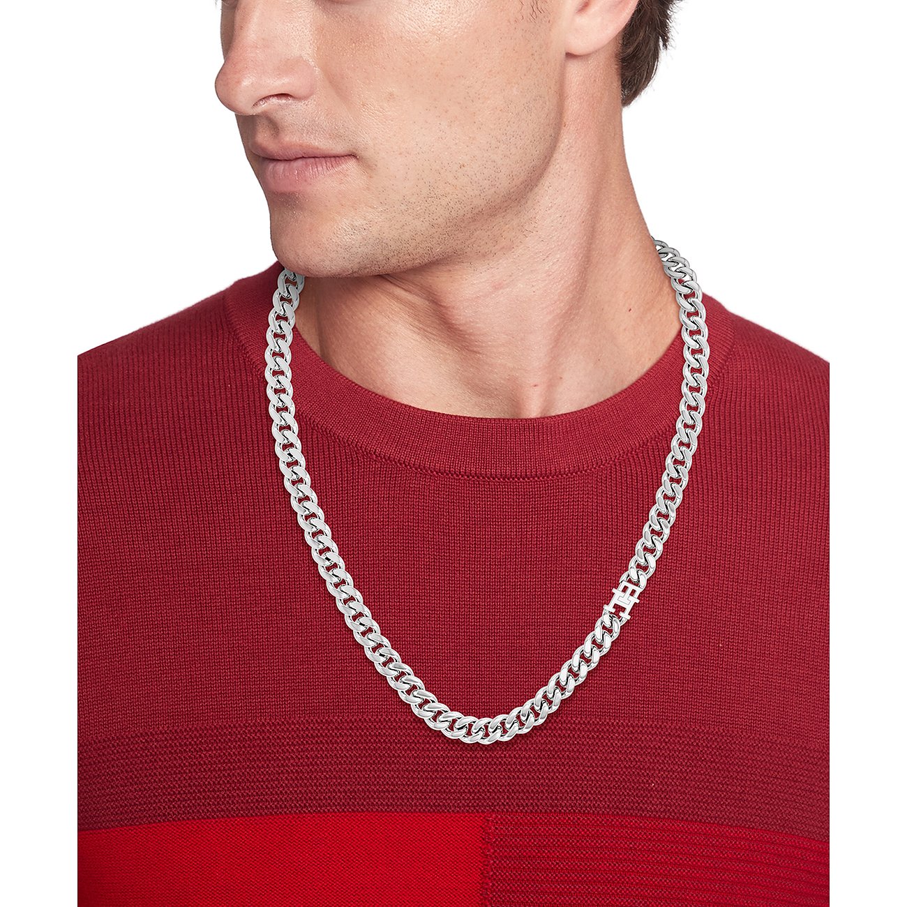Ein Mann im roten Pullover trägt eine glänzende, silberfarbene Tommy Hilfiger Halskette aus Edelstahl.