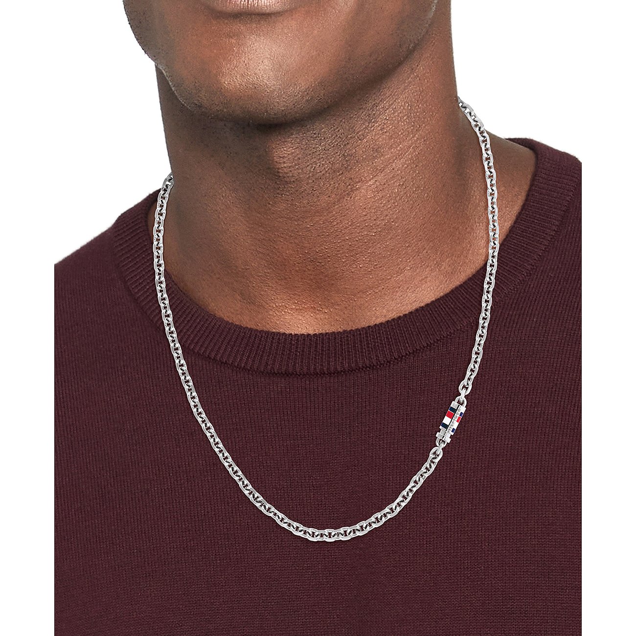 Ein Mann trägt eine Tommy Hilfiger Edelstahlkette mit Gliederkette und rot-weiß-blauer Akzentuierung.