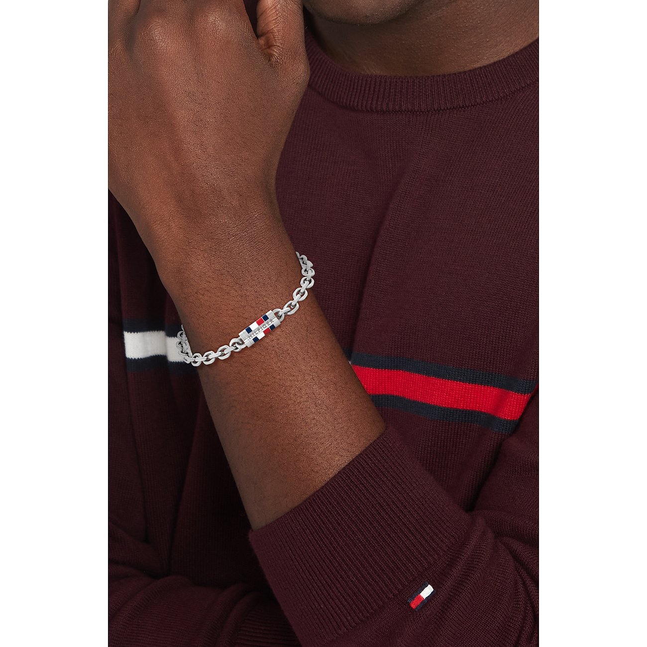Zilveren Tommy Hilfiger roestvrijstalen armband met rood, wit en blauw logo om de pols van een man.