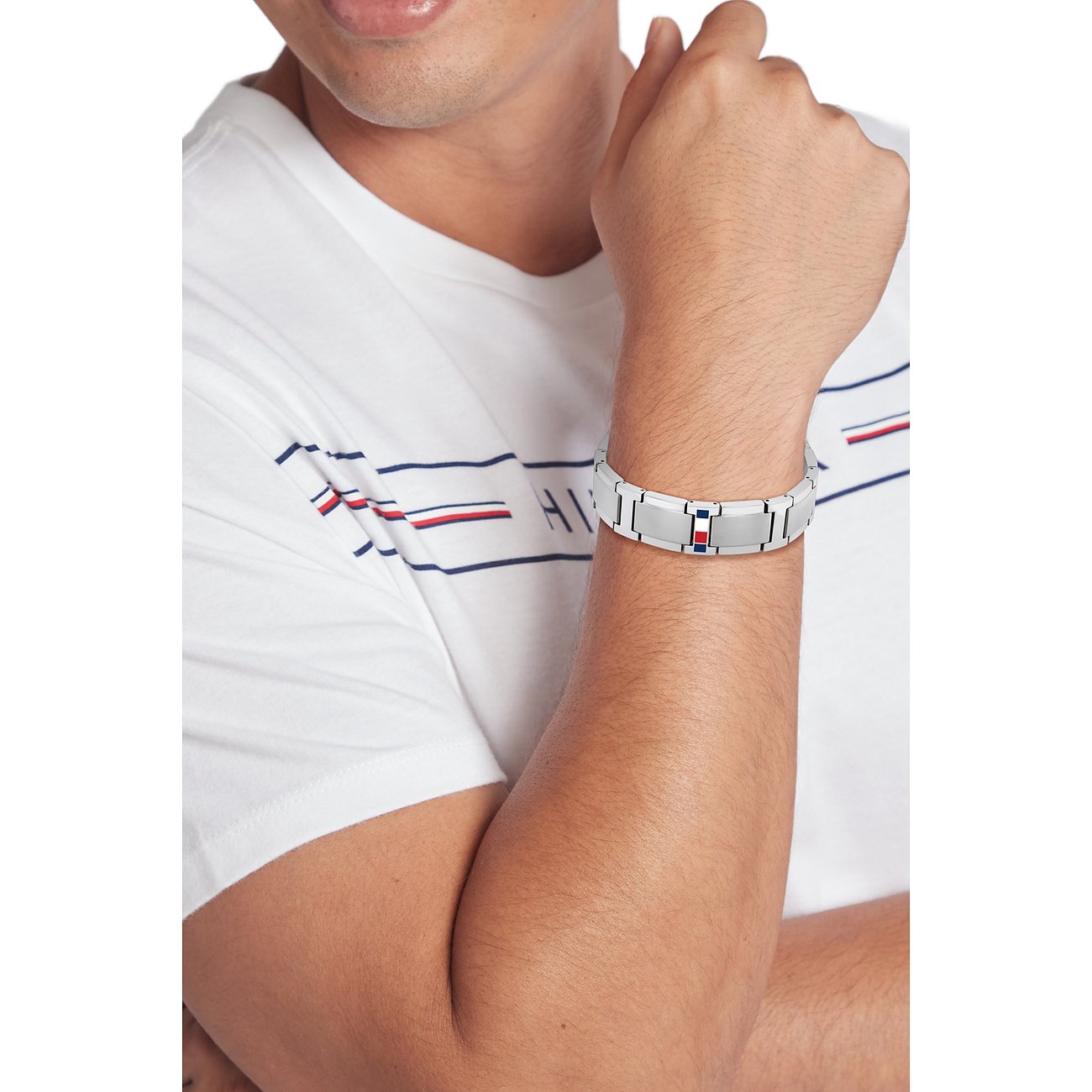Ein Mann trägt die Tommy Hilfiger Herrenarmkette aus Edelstahl mit Tommy Hilfiger-Flaggen-Logo.