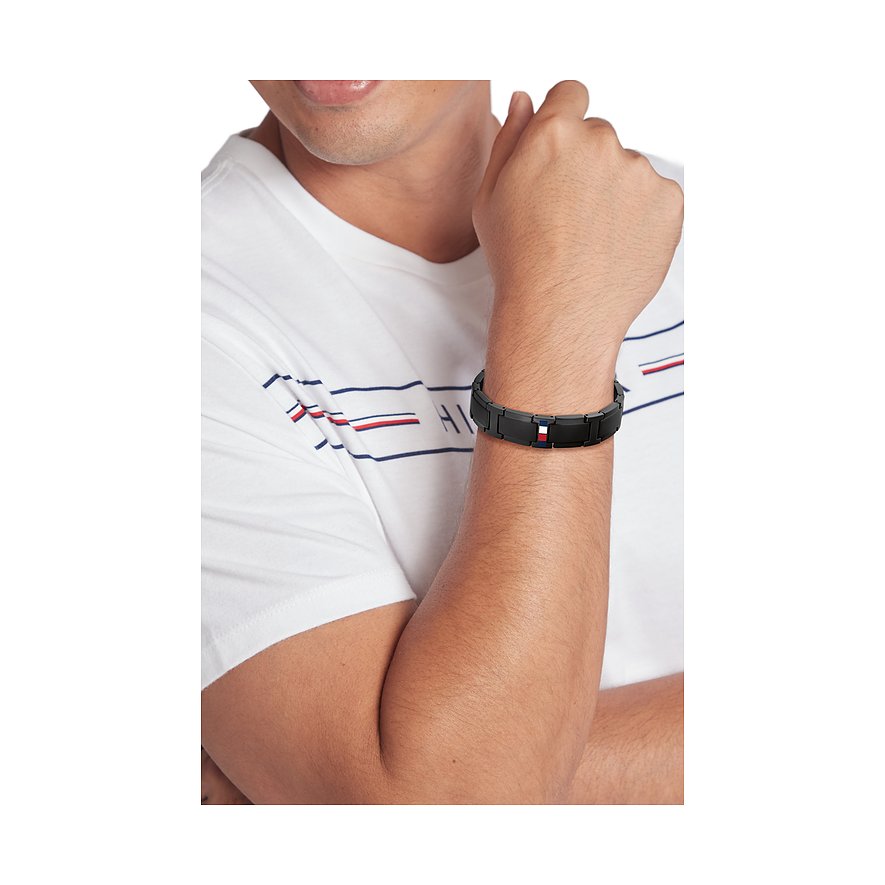 Ein Mann trägt ein schwarzes Armschmuck-Bandarmband aus Edelstahl von Tommy Hilfiger mit Markenlogo in der Mitte.