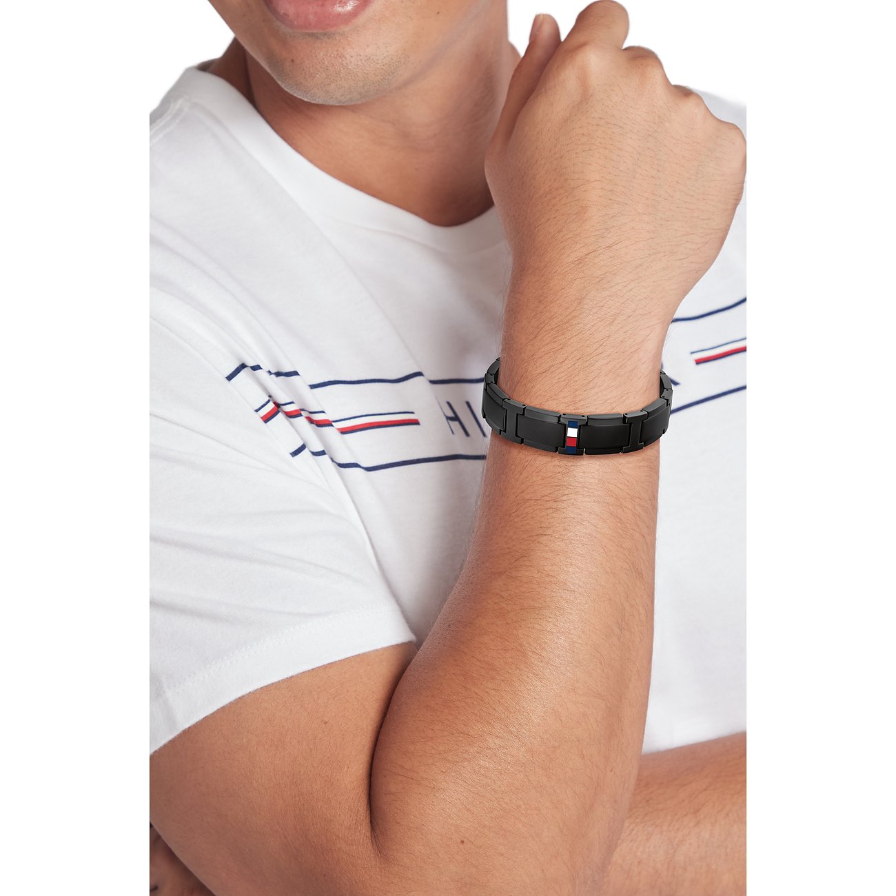 Ein Mann trägt ein schwarzes Armschmuck-Bandarmband aus Edelstahl von Tommy Hilfiger mit Markenlogo in der Mitte.
