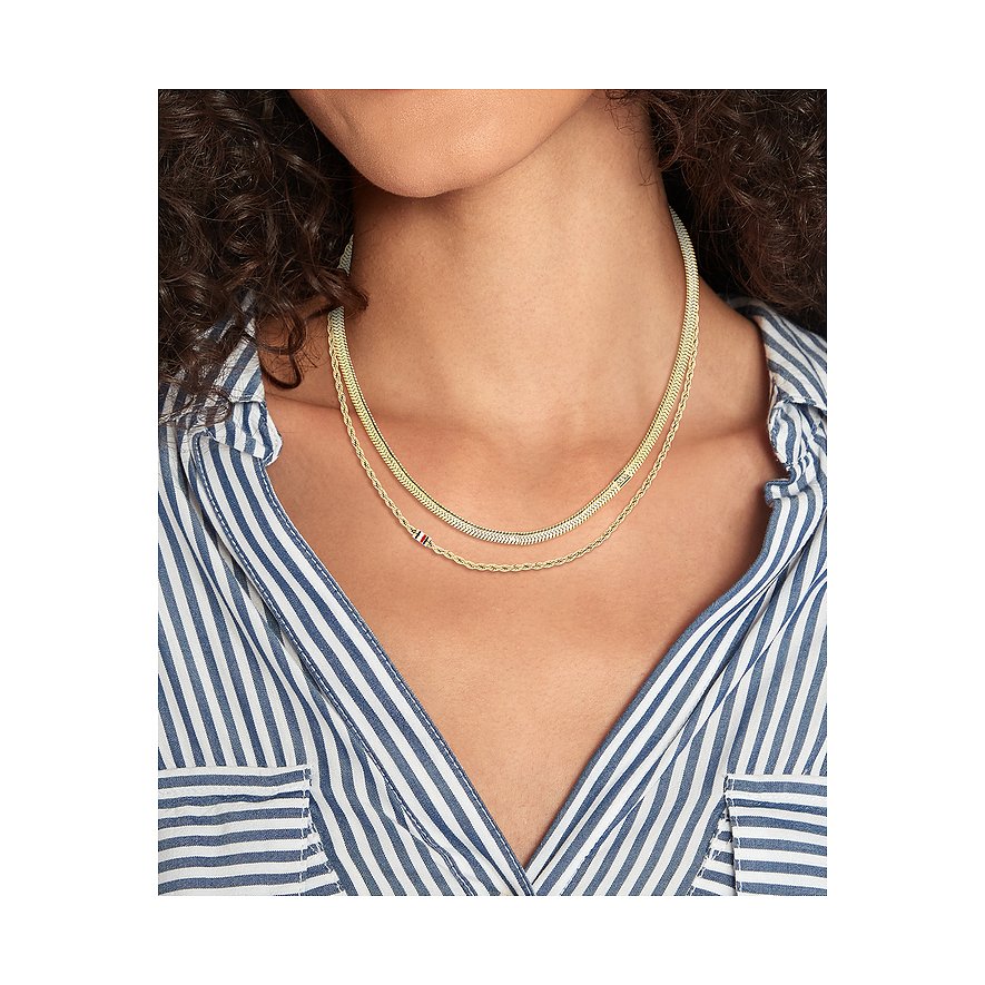 Tommy Hilfiger Halsschmuck aus goldfarbenem Edelstahl. Eine Frau trägt eine mehrreihige Kette auf ihrem gestreiften Hemd.
