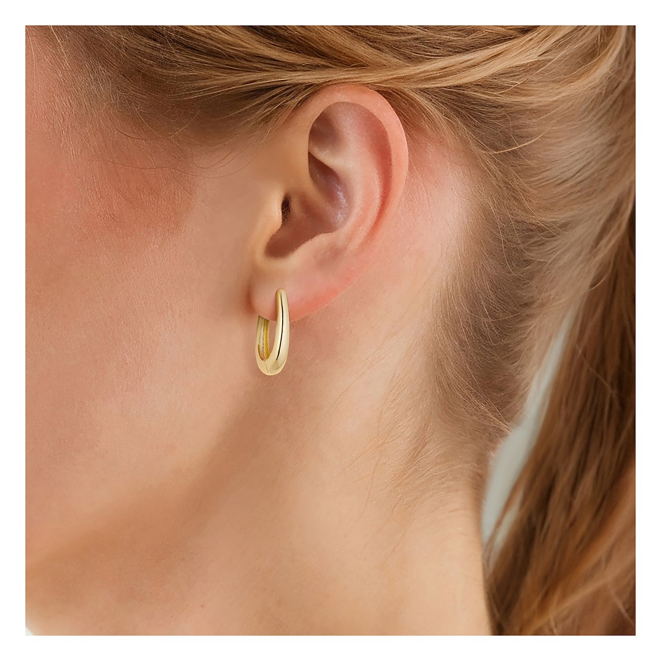 Ein glänzender goldfarbener Ohrring von Glanzstücke München, elegant und fein, getragen am Ohr einer jungen Frau.