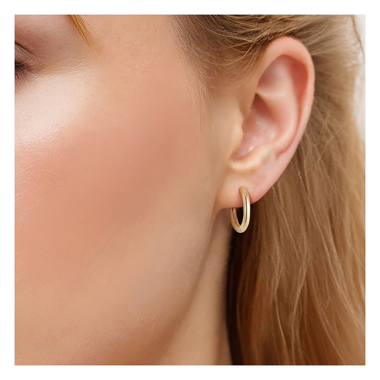 Ein glänzender goldfarbener Glanzstücke München Ohrring aus 925er Silber in Form einer kleinen Creole wird am Ohr getragen.