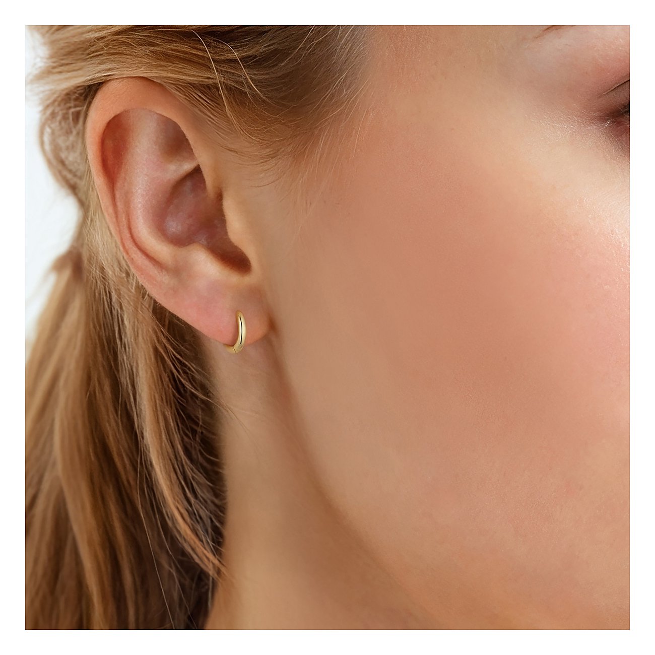 Close-up einer Frau mit einem kleinen, schlichten, goldfarbenen Creolen Ohrschmuck von Glanzstücke München.