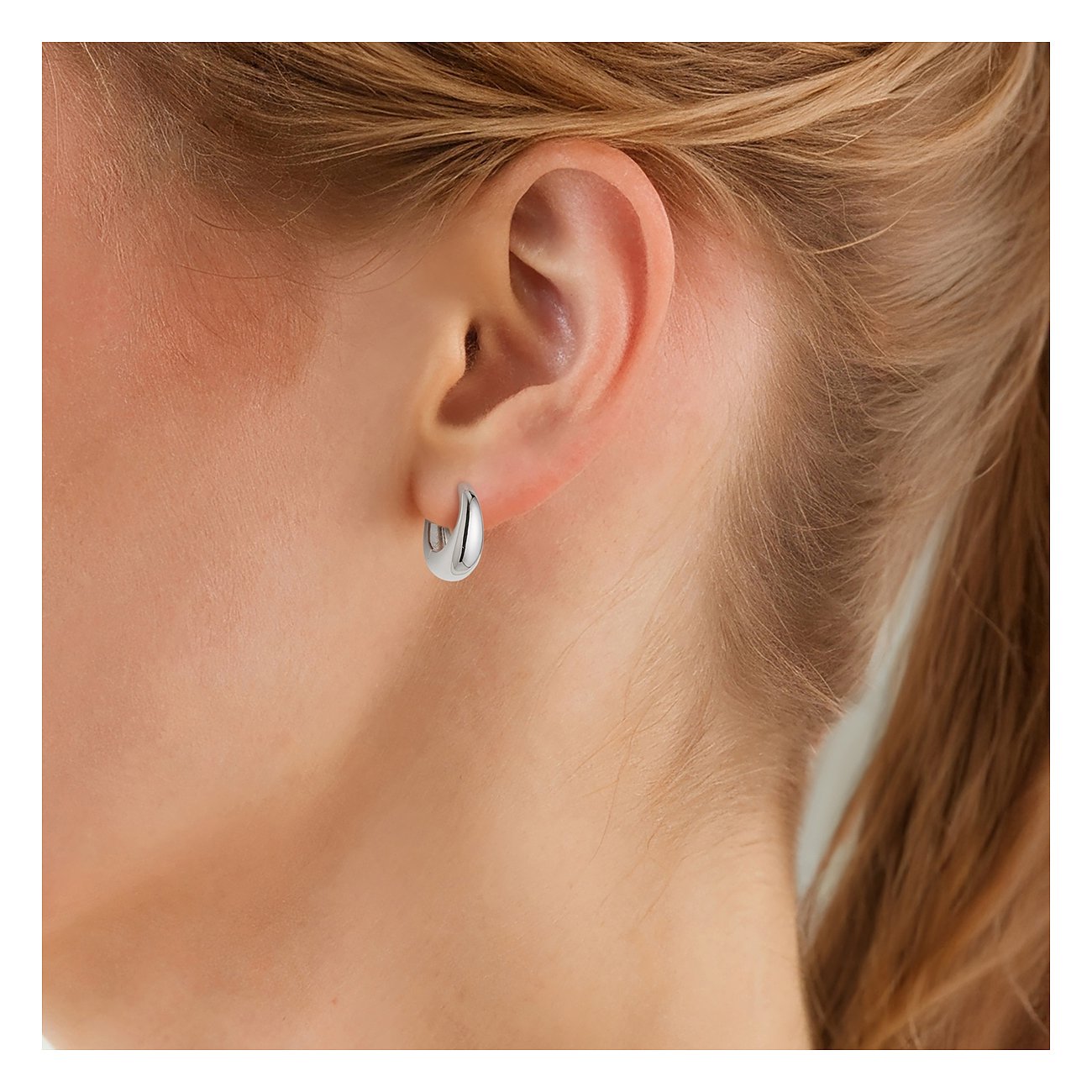 Une boucle d'oreille créole brillante en argent 925 de Glanzstücke München, portée sur une oreille, photographiée de dos.