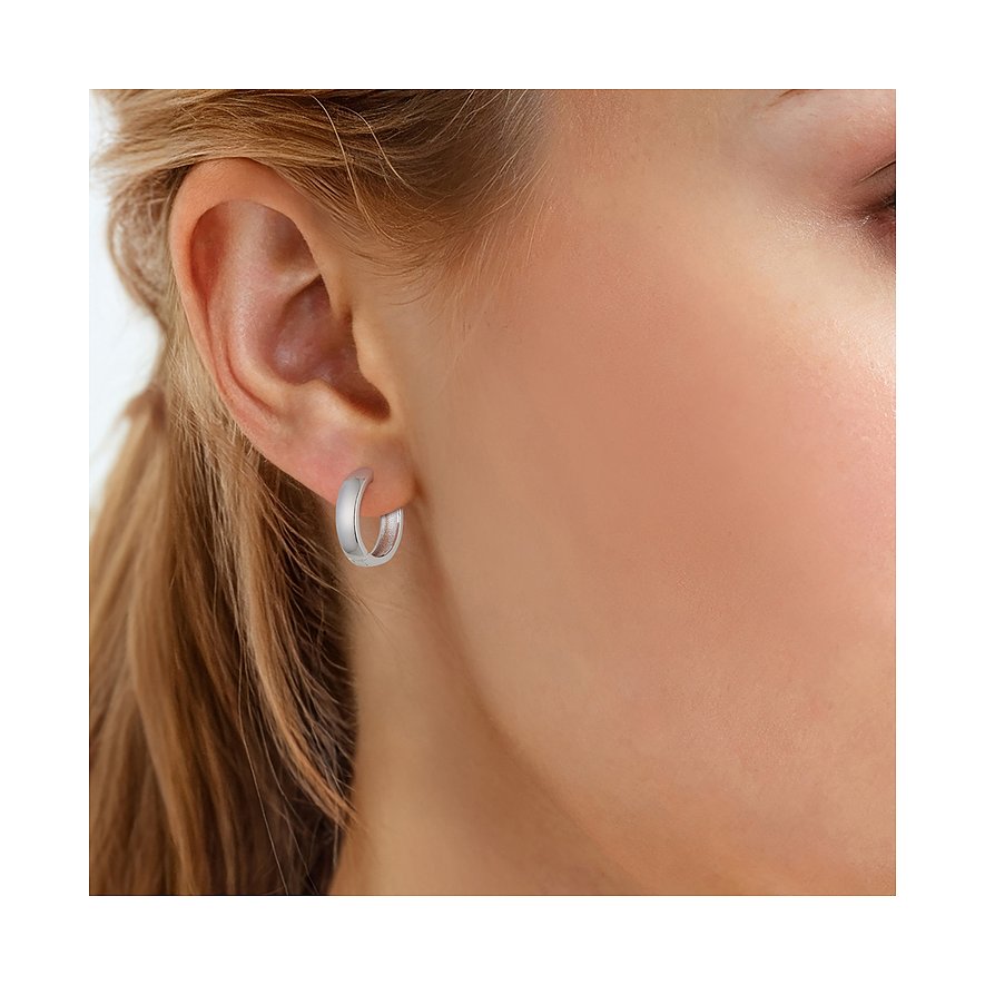 Une boucle d'oreille créole Glanzstücke München en argent 925, finition givrée, portée à l'oreille d'une femme, gros plan.