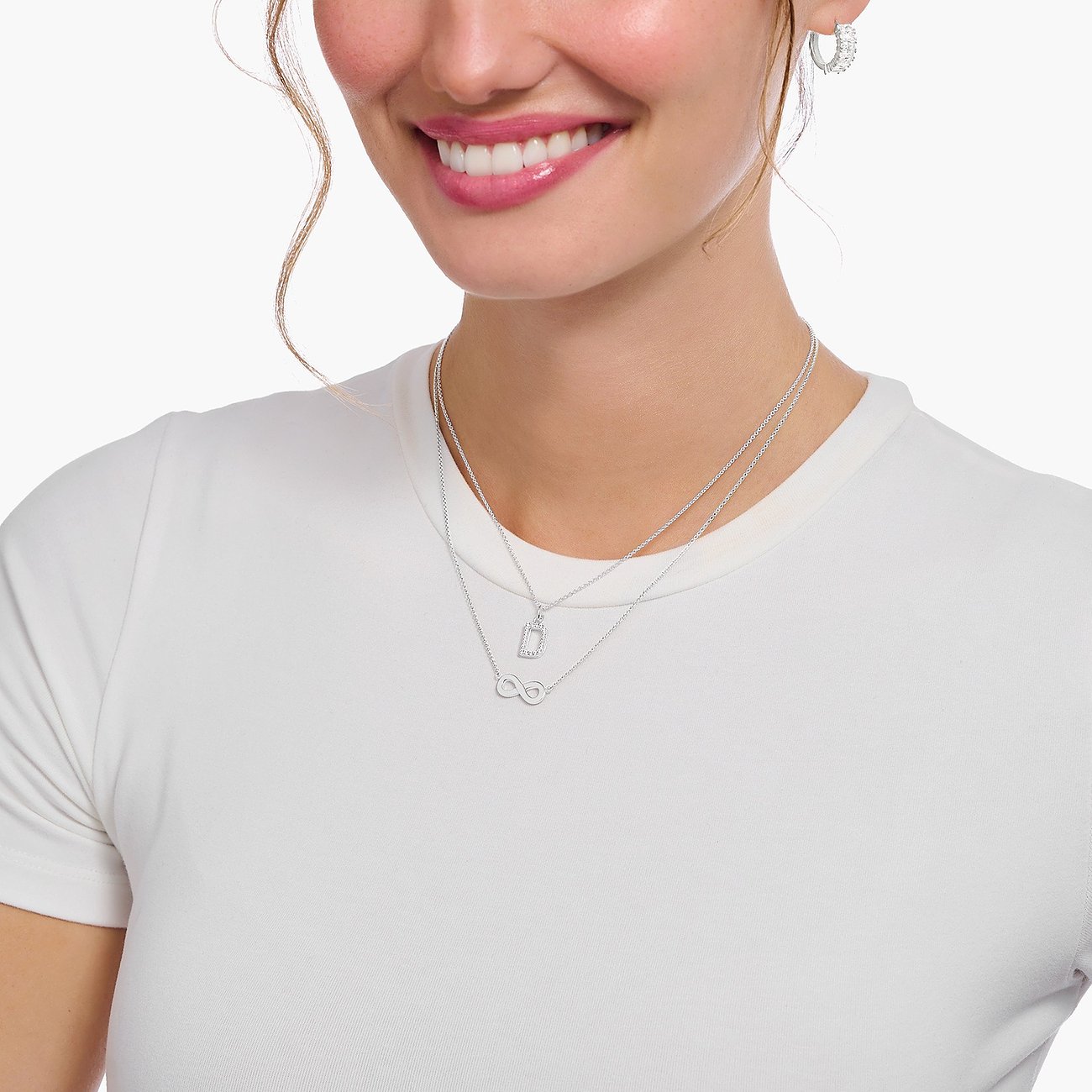 Eine Nahaufnahme einer Frau, die zwei Thomas Sabo Halsketten aus 925er Silber mit Zirkonia-Steinen trägt.