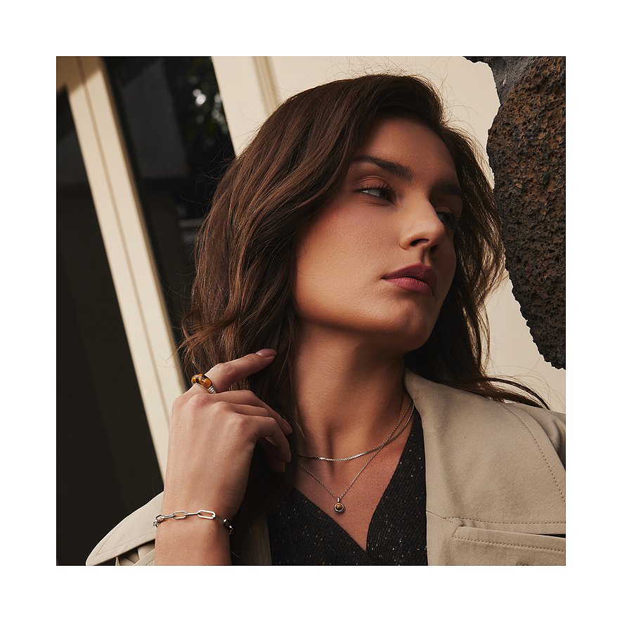 Een vrouw draagt een Ania Haie zilveren ketting met een ronde bruine zirkonia steen hanger en een schakelarmband.