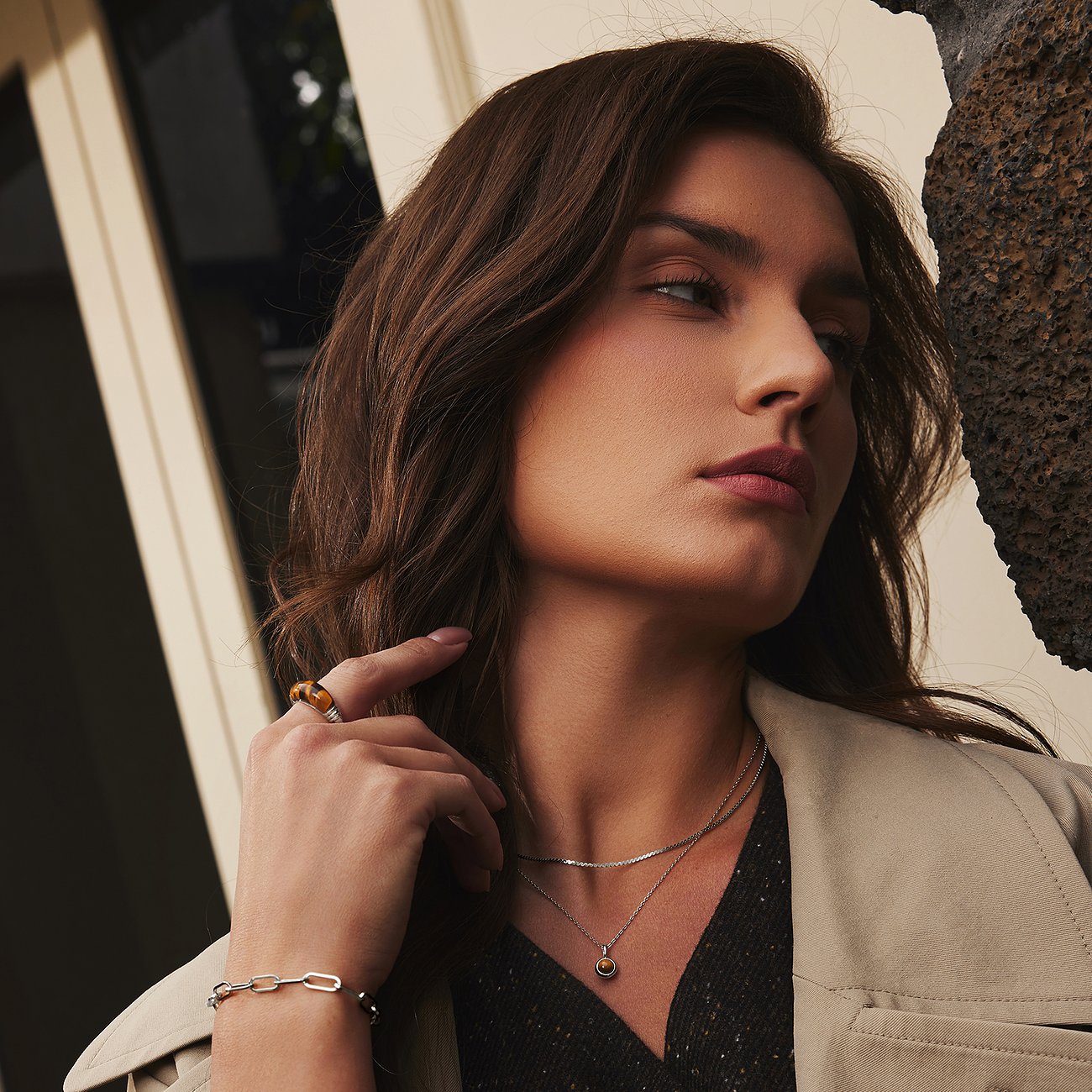 Een vrouw draagt een Ania Haie zilveren ketting met een ronde bruine zirkonia steen hanger en een schakelarmband.