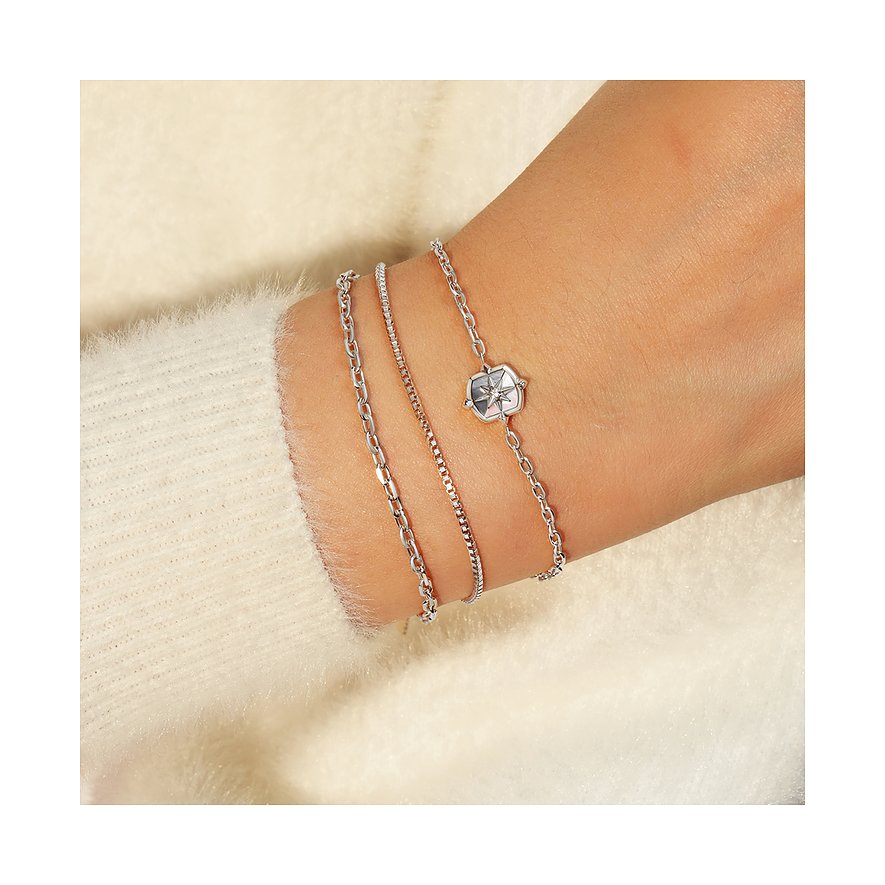 Trois bracelets Ania Haie en argent 925 sur un poignet, l'un avec un pendentif boussole argenté.
