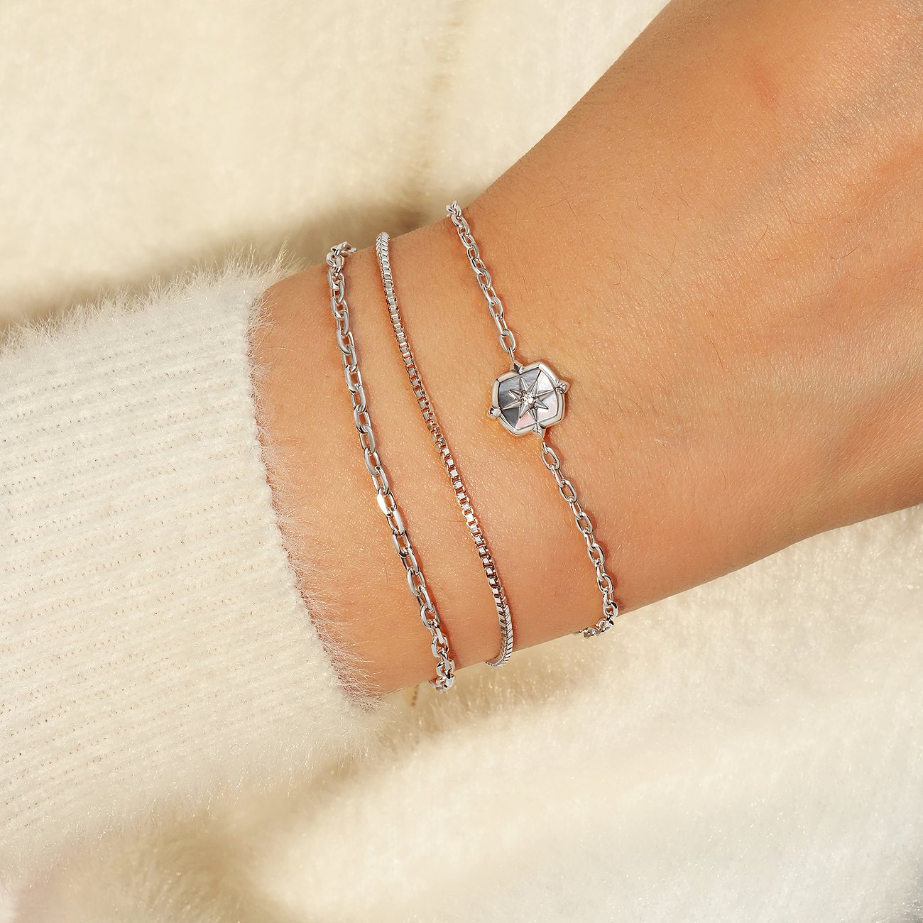 Trois bracelets Ania Haie en argent 925 sur un poignet, l'un avec un pendentif boussole argenté.