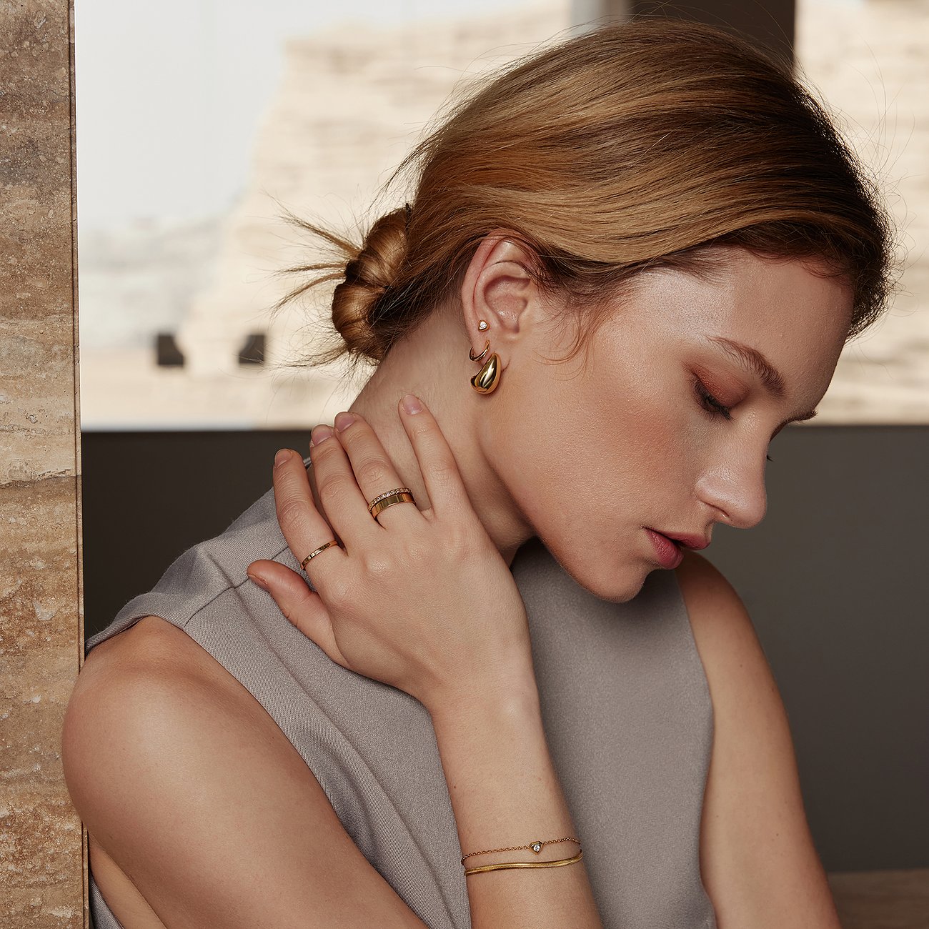 Gros plan d'une femme portant de larges boucles d'oreilles Ania Haie dorées brillantes et une bague assortie fine.
