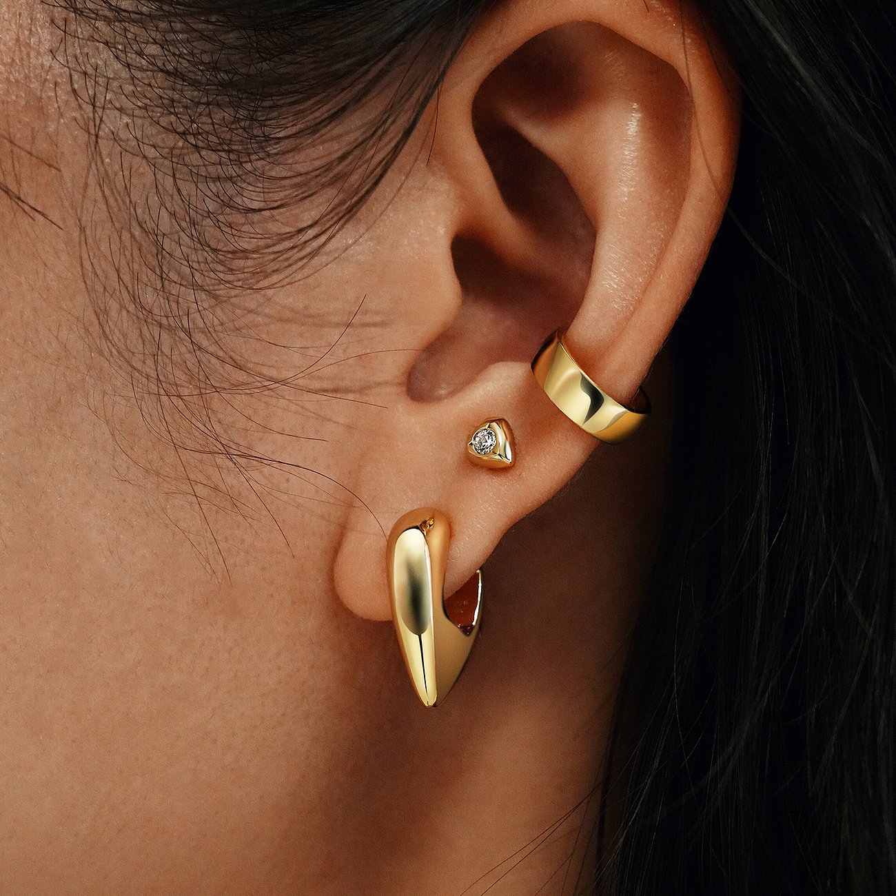 Nahaufnahme-Ohr eines Models mit mehreren Ania Haie Ohrringen aus 925er Silber, inklusive goldenem Creolen-Ohrschmuck