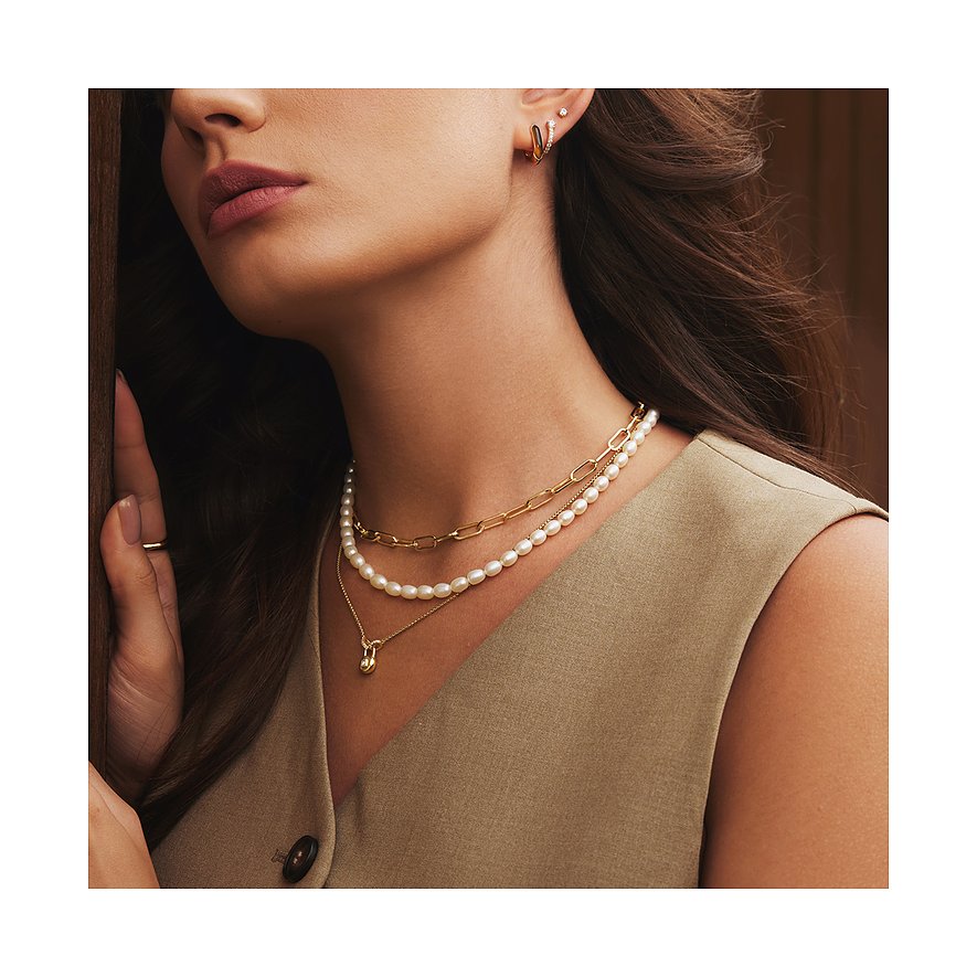 Närbild av en kvinna som bär två Ania Haie halsband, tittar fundersamt åt sidan.