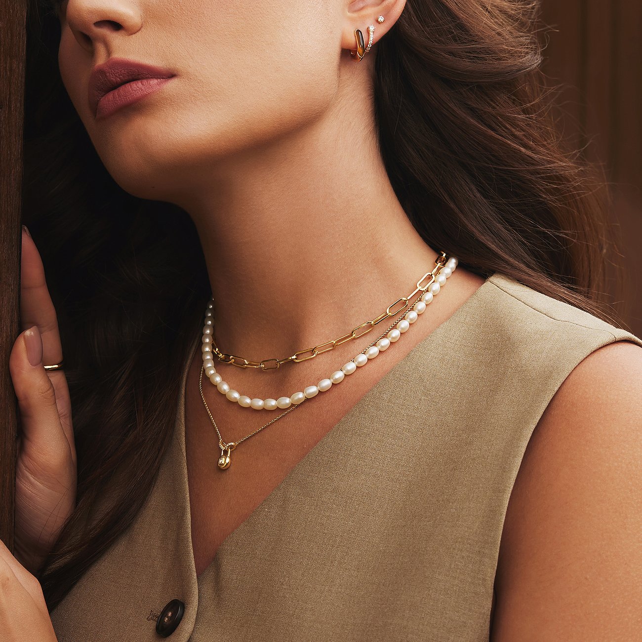 Närbild av en kvinna som bär två Ania Haie halsband, tittar fundersamt åt sidan.