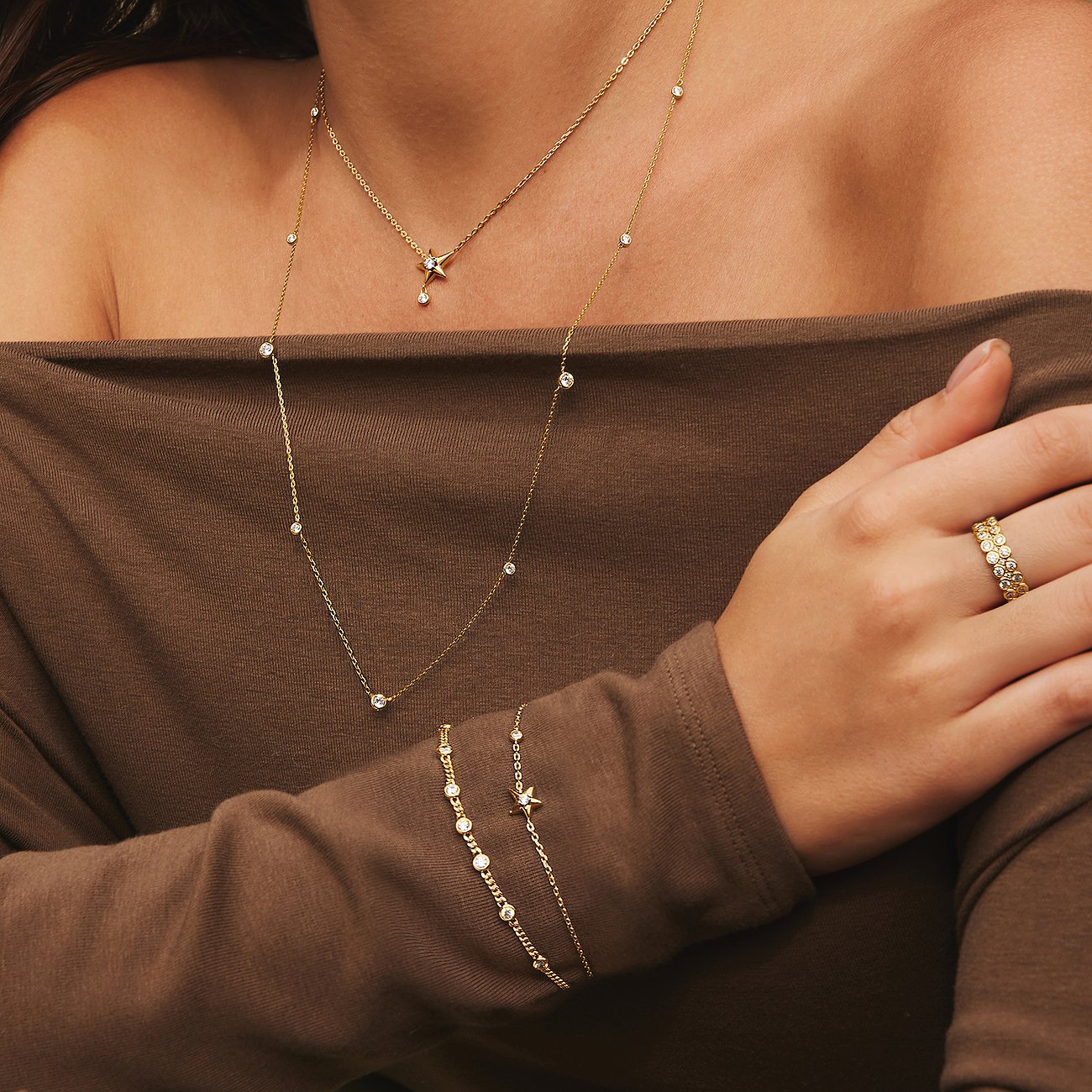 Le mannequin porte des bijoux de bras Ania Haie en argent plaqué or avec zircone, collier et bague assortis.
