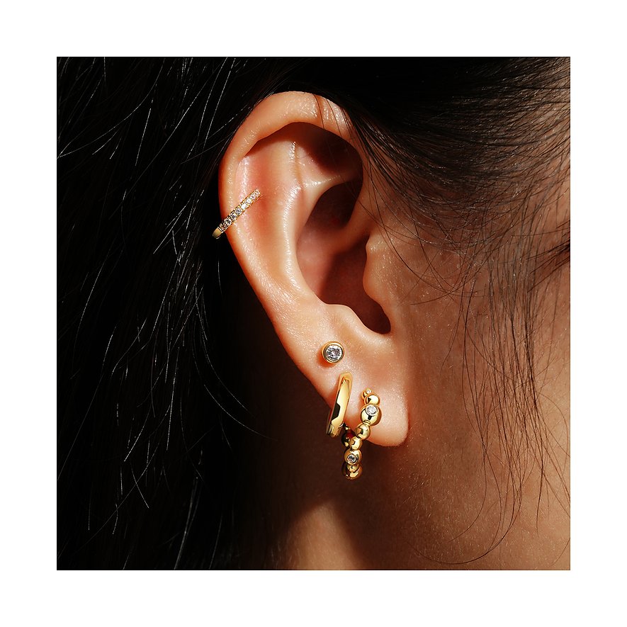 Gros plan d'une oreille avec plusieurs boucles d'oreilles Ania Haie, dont une créole argentée ornée de zircones colorés.