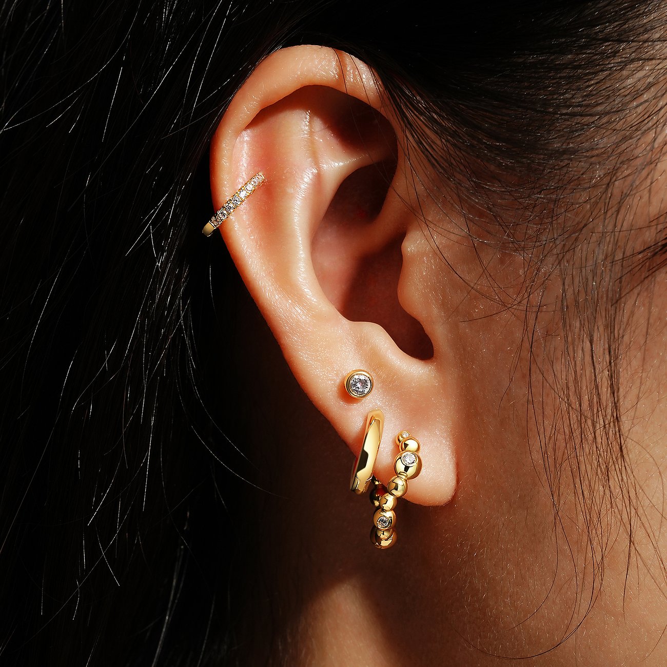 Gros plan d'une oreille avec plusieurs boucles d'oreilles Ania Haie, dont une créole argentée ornée de zircones colorés.