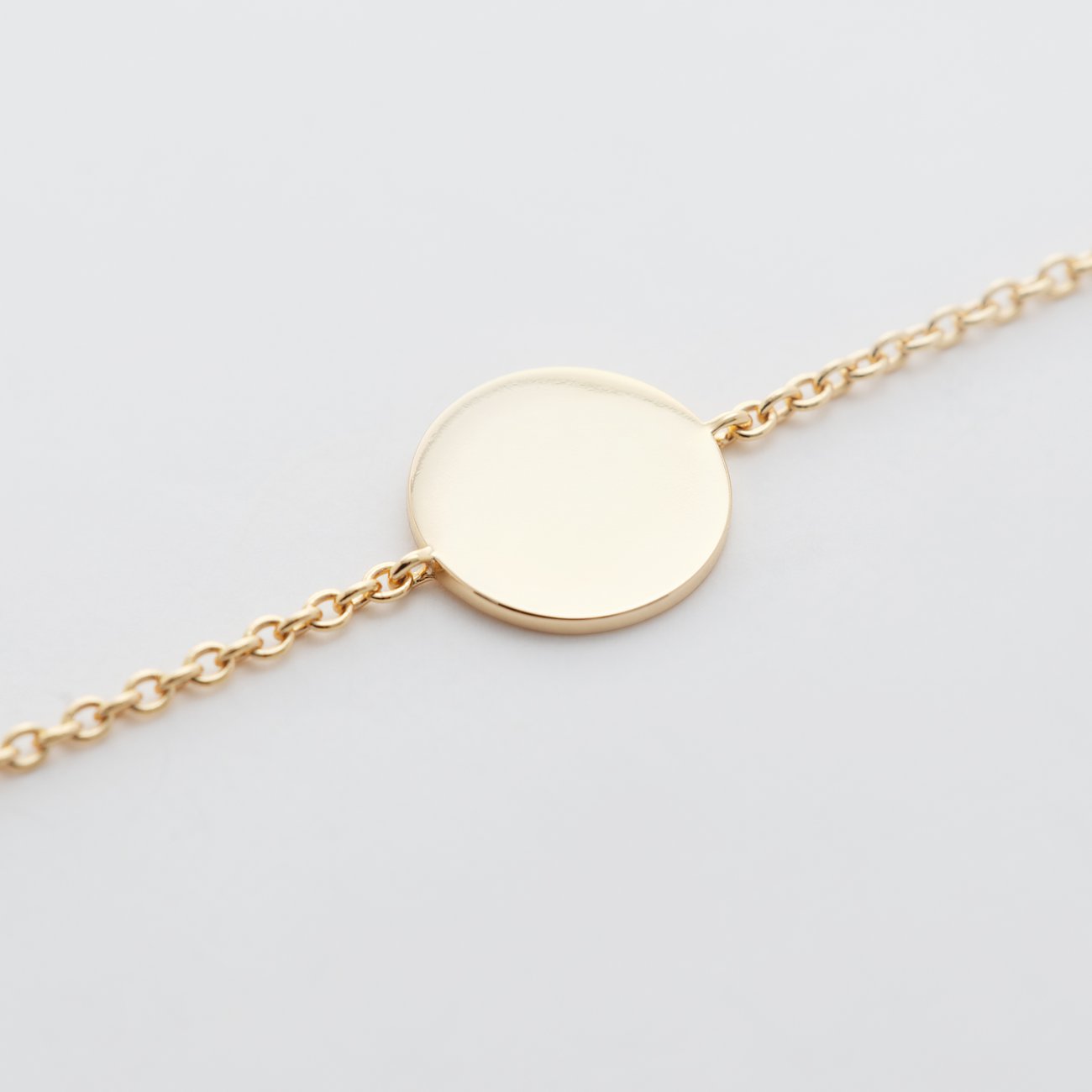 FAVS Armschmuck in Silber. Ein schmaler, goldfarbener Kettenarmschmuck in Nahaufnahme mit einem runden Anhänger.