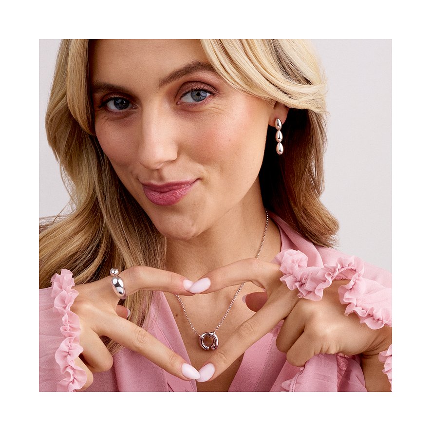 Eine Frau l&aumlchelnd, eine Sif Jakobs Jewellery Ohrschmuck aus Silber tragend, die H&aumlnde zu einem Herz geformt.