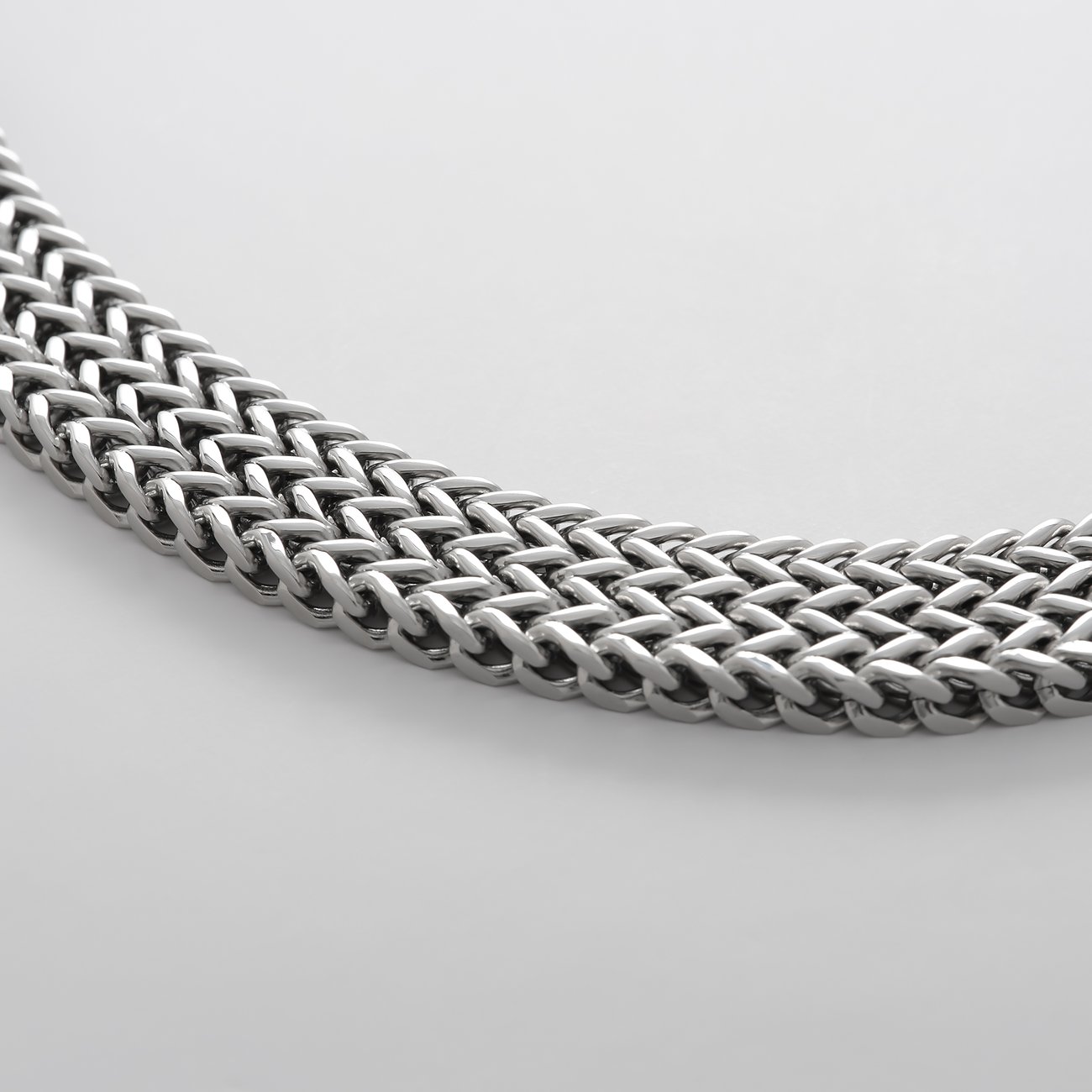 Detailaufnahme des FAVS Armschmucks aus Edelstahl in Form einer breiten, flachen Kette mit eng verflochtenen Gliedern.