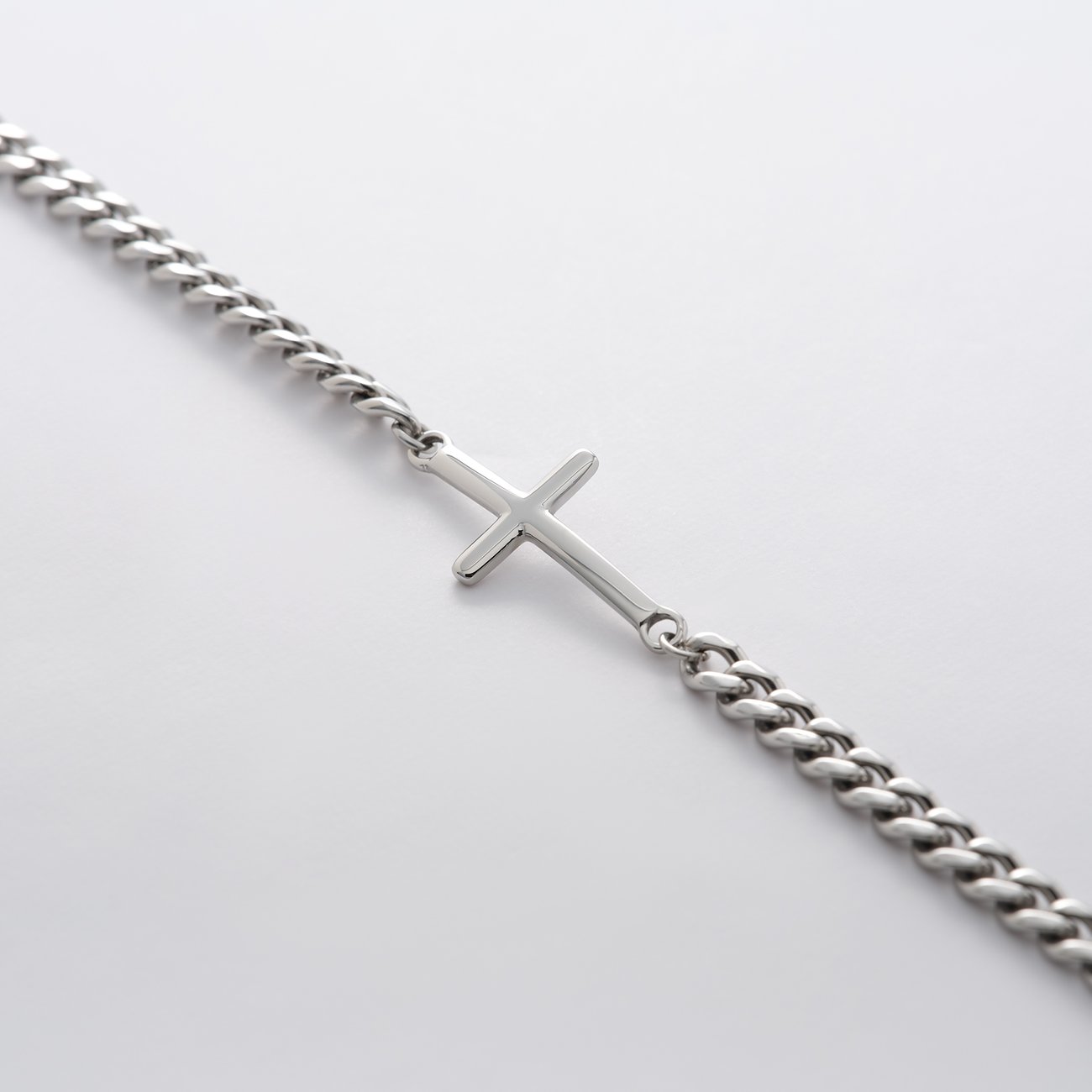 FAVS roestvrijstalen armband met een eenvoudige kruishanger, schuin liggend op een witte achtergrond.