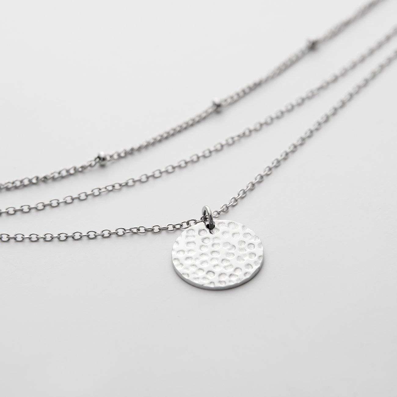 FAVS Halsschmuck: dreireihige Kette aus Edelstahl mit einem gehämmerten runden Plättchen in der Mitte.