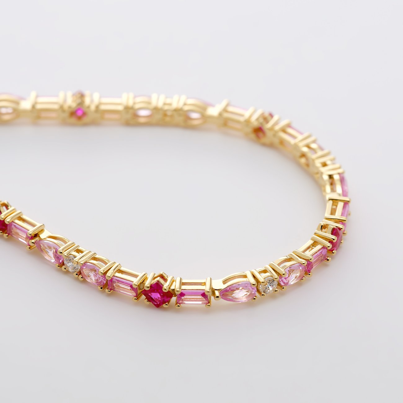 Nahaufnahme eines goldfarbenen Armbands von CHRIST aus recyceltem 925er Silber mit rosa und roten Zirkonia Farbsteinen.