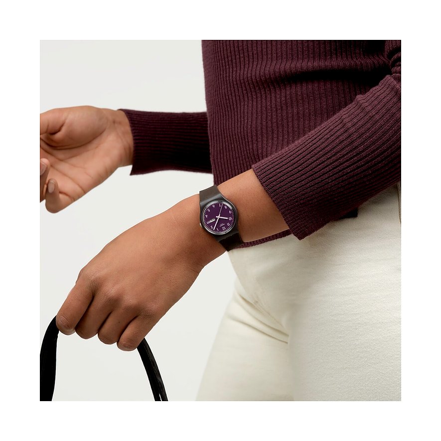 Eine Nahaufnahme einer Swatch Unisexuhr aus Kunststoff an einem Handgelenk, mit lilafarbenem Zifferblatt.