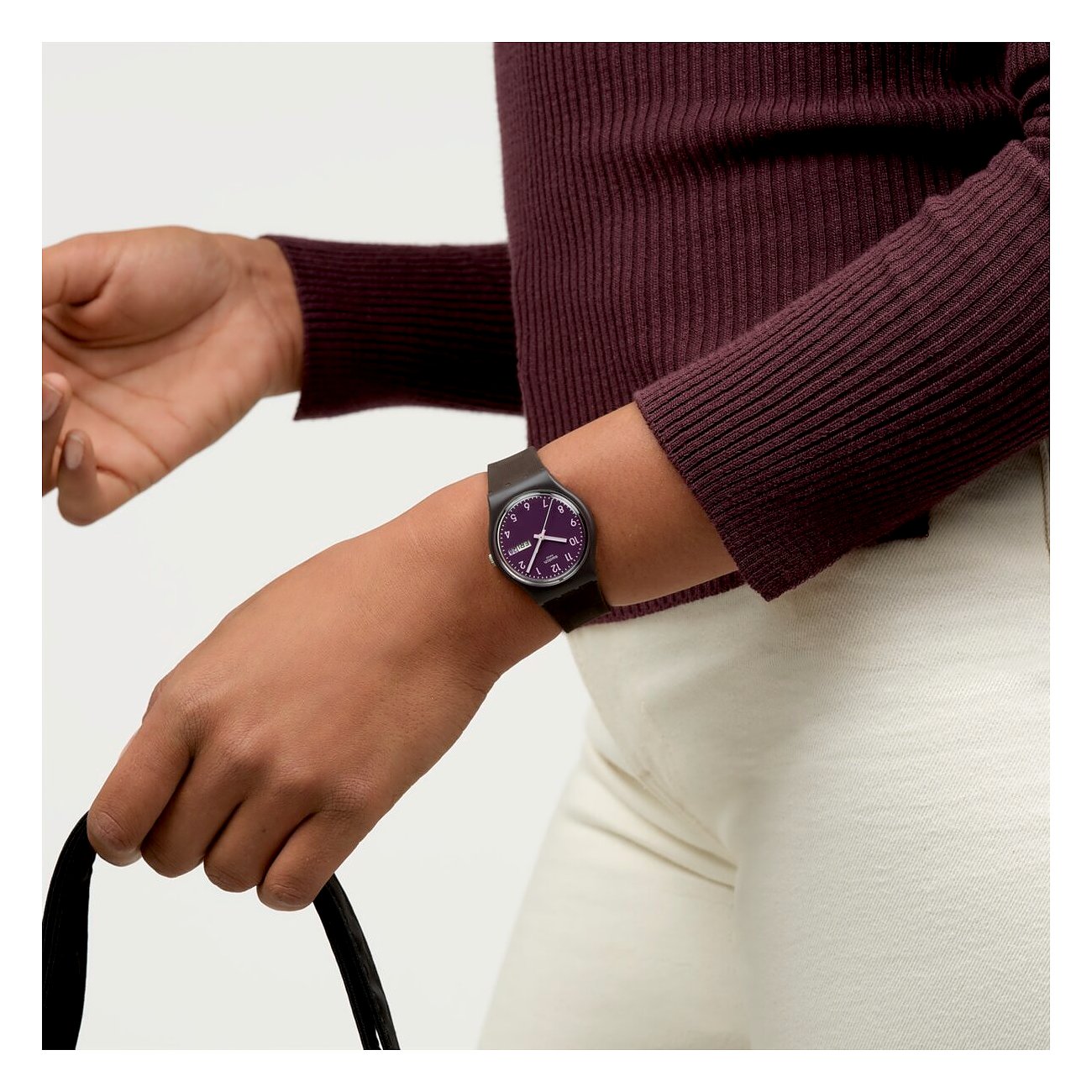 Eine Nahaufnahme einer Swatch Unisexuhr aus Kunststoff an einem Handgelenk, mit lilafarbenem Zifferblatt.
