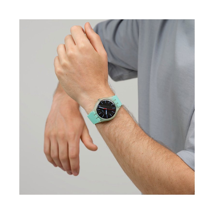 Am Handgelenk eines Mannes getragene Swatch Unisexuhr aus Kunststoff in Minzgrün und Schwarz in Nahaufnahme.