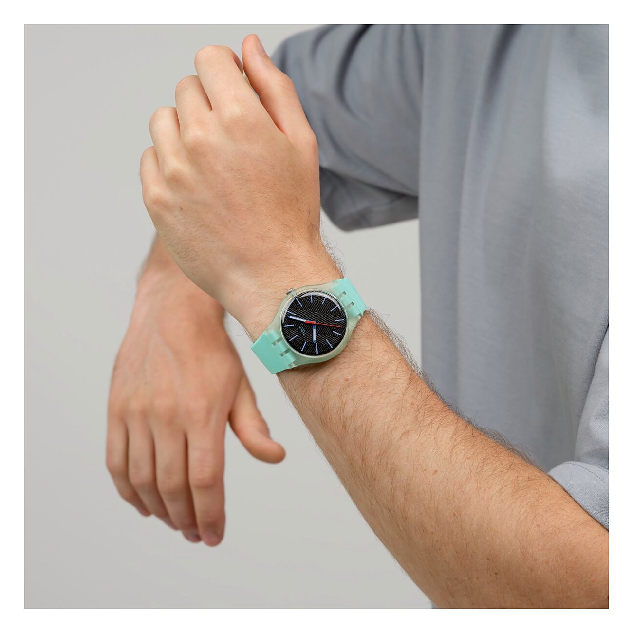 Am Handgelenk eines Mannes getragene Swatch Unisexuhr aus Kunststoff in Minzgrün und Schwarz in Nahaufnahme.