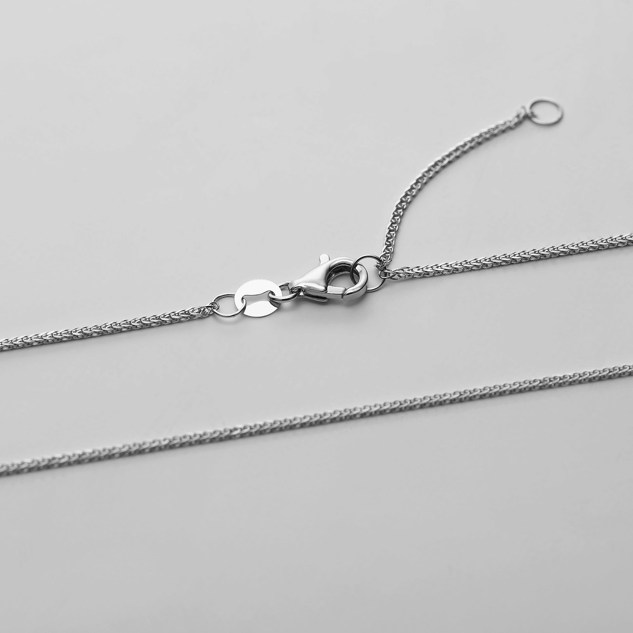 Nahaufnahme der Schließe einer Weißgoldkette des CHRIST Halsschmucks, die auf einem grauen Hintergrund liegt.