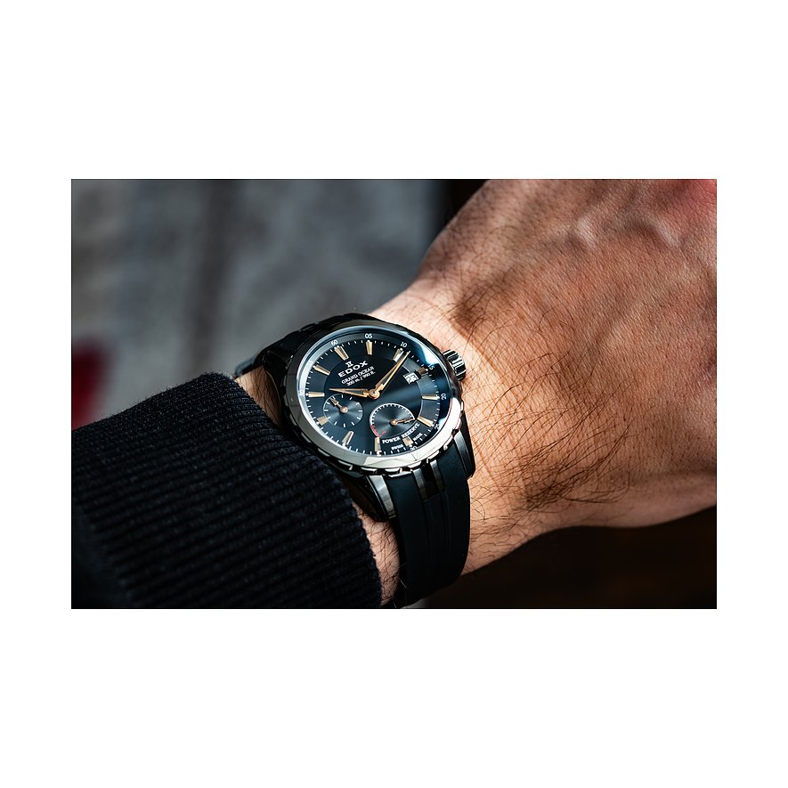 Die Edox Herrenuhr aus Edelstahl und Aluminium mit schwarzem Zifferblatt und Kautschukarmband wird am Handgelenk getragen.