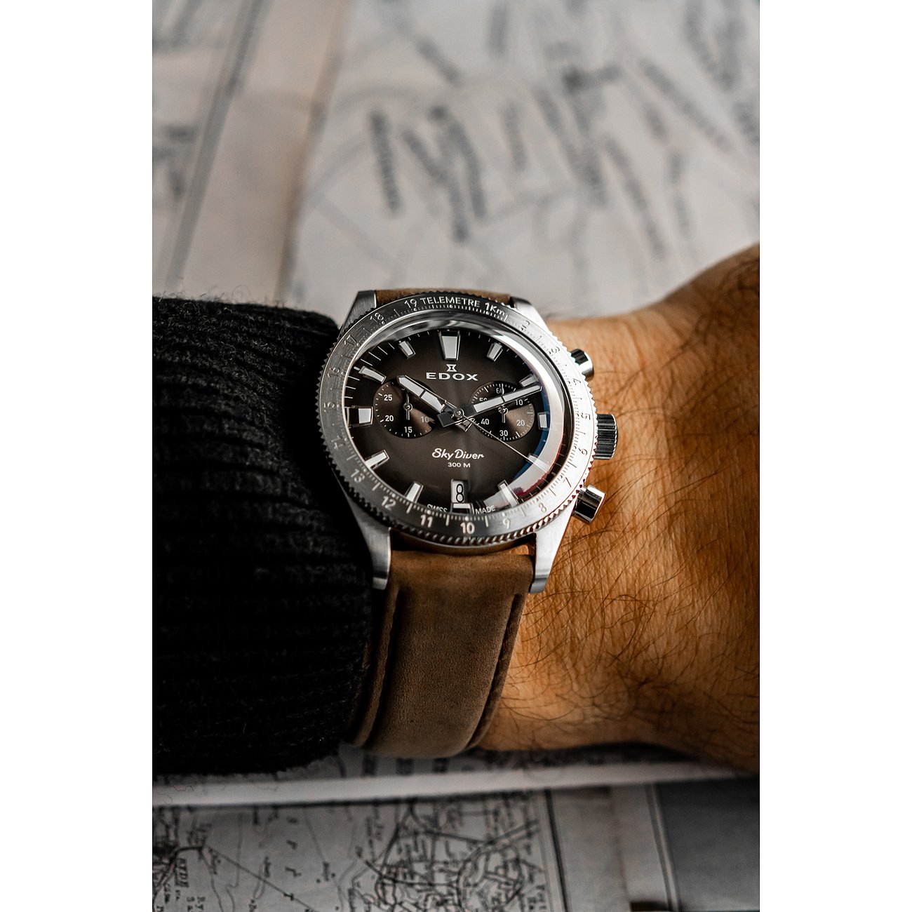 Am Handgelenk getragene Edox Sky Diver Herrenuhr aus Edelstahl und Aluminium mit braunem Uhrband.