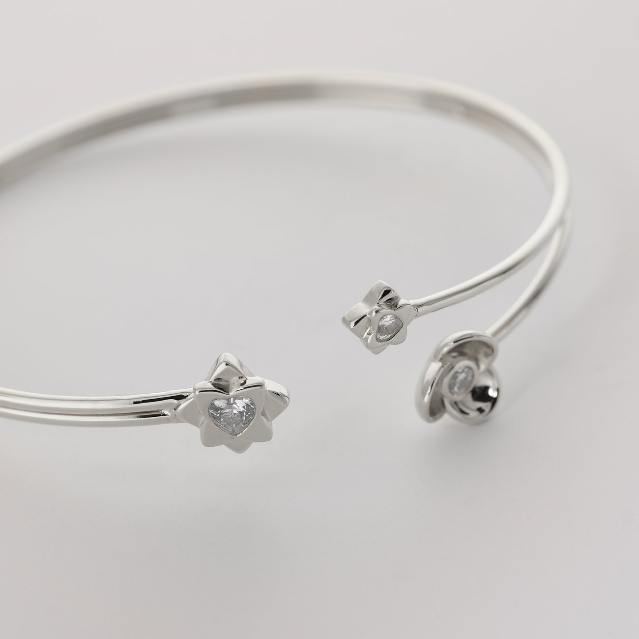 Nahaufnahme eines JETTE Armreifs aus recyceltem 925er Silber mit Zirkonia-Verzierung in Blüten- und Herzform.