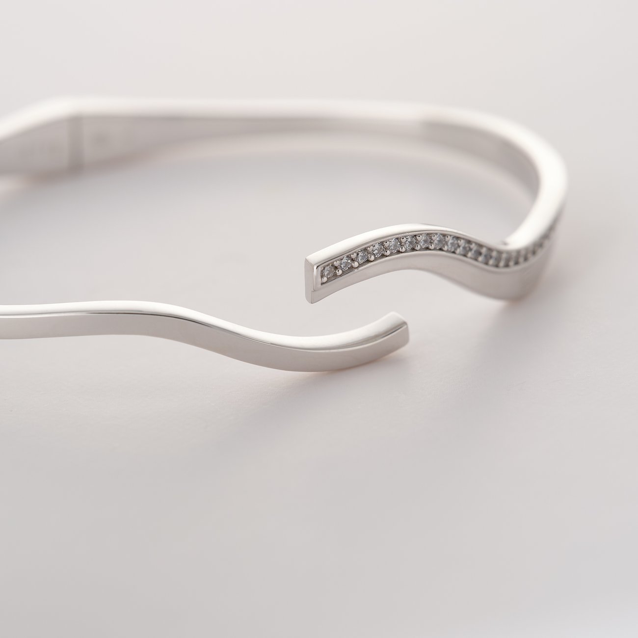 Nahaufnahme eines JETTE Armreifs aus recyceltem 925er Silber mit Zirkonia-Steinen in einer wellenförmigen Reihe.