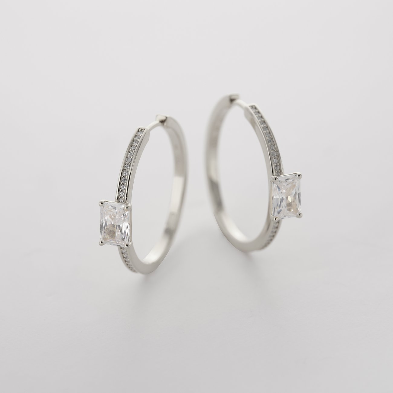 Un paio di orecchini a cerchio JETTE in argento riciclato 925 con zirconi e uno zircone rettangolare.