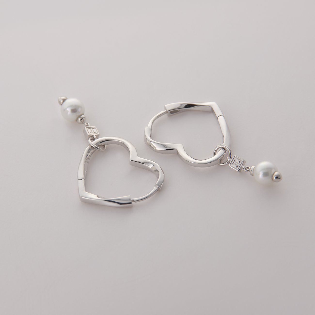 Zwei herzförmige JETTE Ohrringe aus recyceltem Silber mit jeweils einer baumelnden Perle.