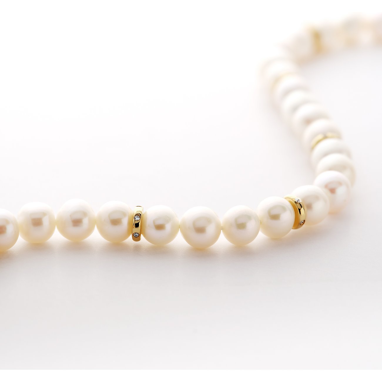 Close-up van een CHRIST 585 geelgouden parelketting, met parels onderbroken door gouden ringen met edelstenen.