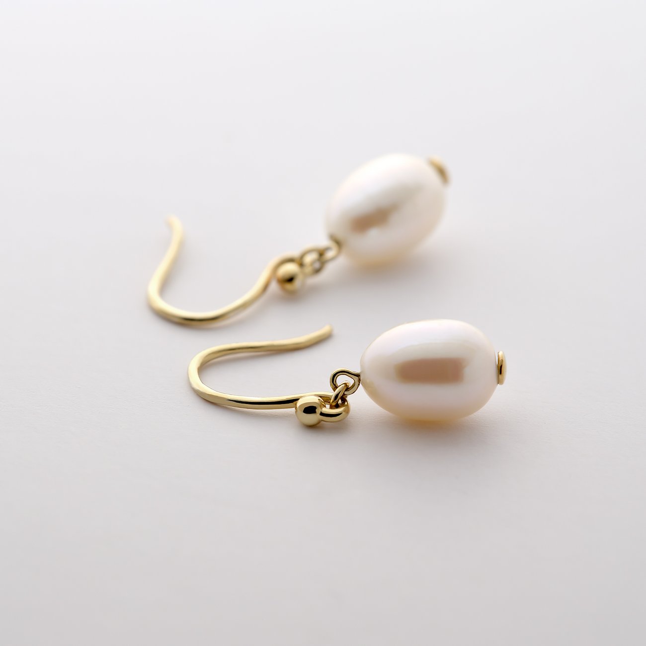 Boucles d'oreilles CHRIST en or jaune avec perles en forme de goutte, vue du dessus sur une surface blanche.
