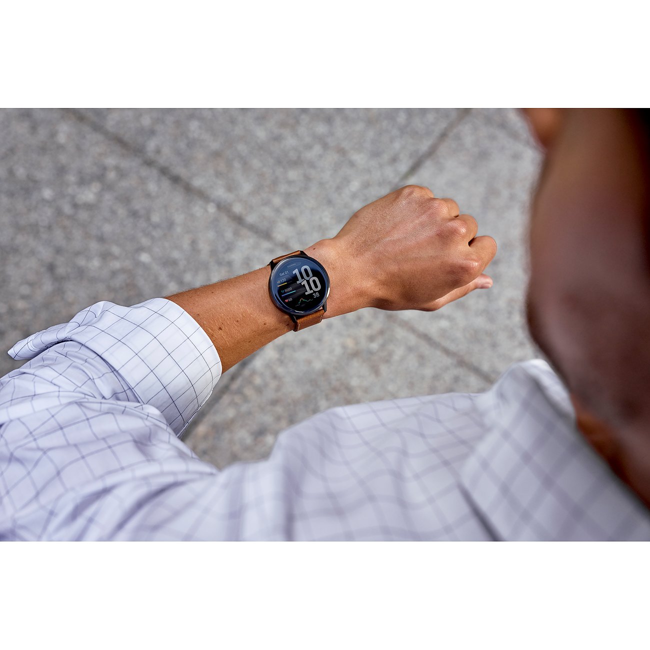 Nahaufnahme einer Garmin Smartwatch mit braunem Kunststoffarmband am linken Handgelenk eines Mannes, der auf die Uhrzeit schaut.